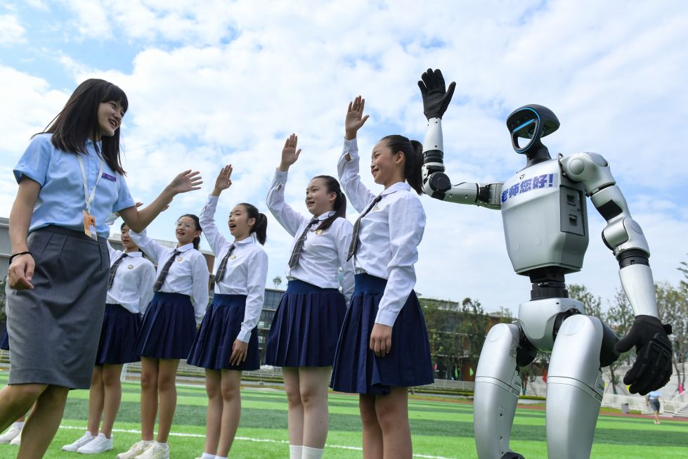 2025年9月9日，在四川师范大学附属生物城学校操场，一台人形机器人和学生一起向老师问好，祝老师教师节快乐。 新华社发（李向雨摄）