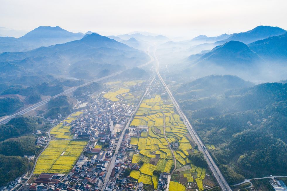 2025年4月2日，在浙江省杭州市临安区天目山镇横塘村，油菜花田与村庄、公路、群山构成一幅美丽画卷（无人机照片）。新华社发（胡剑欢摄）